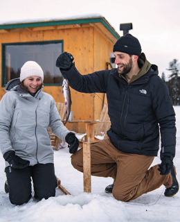 Un couple faisant de la pêche blanche sur un lac glacé.