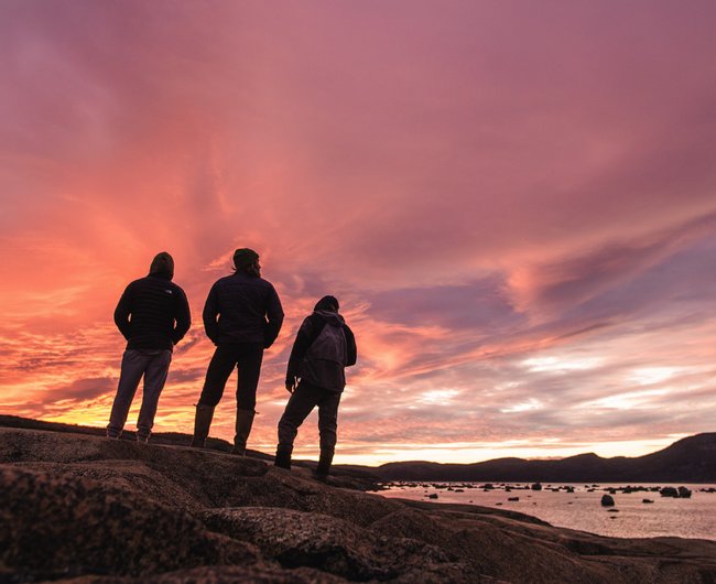 Three people standing under a pink sunset